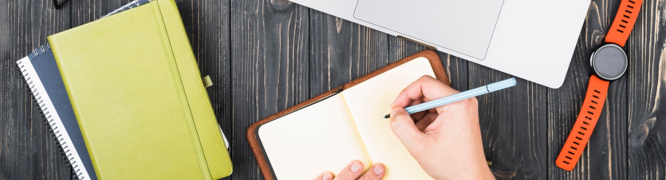 une personne écrit sur un carnet devant un ordinateur portable 